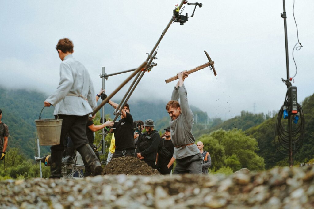 Film crew setting up a historical scene with actors outdoors in nature.
